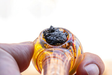 glass marijuana weed pipe held by hand after consuming it. Closeup first person view of man smoking marijuana weed pipe. Burnt marijuana weed close-up. consumption of weed in a pipe