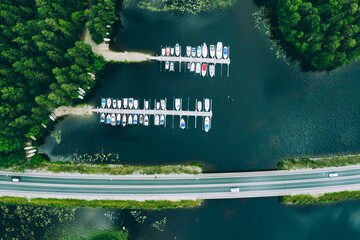 Wall Mural - Aerial view of road with cars between green forests and blue lakes with marina boats in Finland