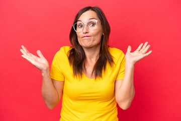 Wall Mural - Middle-aged caucasian woman isolated on red background having doubts while raising hands