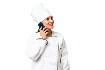 Wall Mural - Middle-aged chef woman over isolated background keeping a conversation with the mobile phone with someone