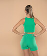 © vladimirfloyd - Fit woman posing indoors. Healthy young female athlete dwearing green sport outfit on a beige background. Back, rear view