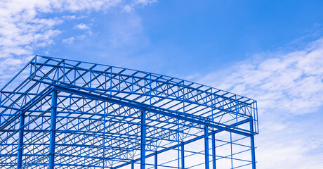 Wall Mural - Low angle view of metal roof beam and columns of new warehouse building structure in construction site area against blue sky background