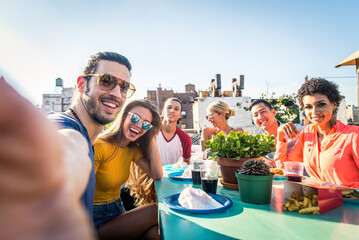 Multiethnic group of young happy friends bonding and having party at home on a rooftop terrace with New York city view