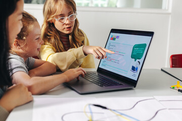 girl explains robot programming code to classmates on a laptop