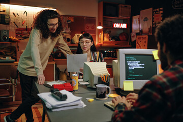 Young people discussing business plan together sitting at table with computers in garage