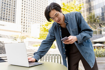 Wall Mural - Portrait of young asian manager using laptop, holding mobile phone, working at workplace outdoors