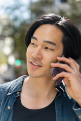 Wall Mural - Closeup portrait of attractive asian man holding mobile phone, talking, looking away