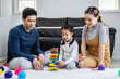 © TeTe Song - Happy asian family father and mother with little asian girl smiling playing with building tower from wooden blocks, taking tiles in turn from underneath until it falls, in moments good time at home