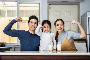 Happy family having fun in the kitchen. Asian Father, mother and little daughter spending time together and having breakfast drinking and hold glasses of milk at table