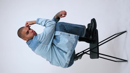 Wall Mural - Thoughtful black guy in denim clothes posing while sitting at the metal back of a chair. High quality 4k footage