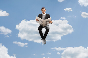 Canvas Print - Professional young man in a suit sitting on a cloud and reading a newspaper