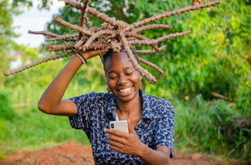 excited young African girl carrying wood and a and using her phone on a farm