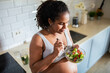 © Baba Images - Young pregnant latina woman eating a salad in the kitchen of a home