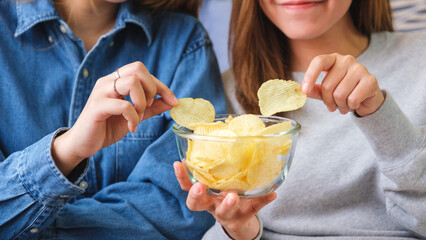 Closeup image of a young couple women sharing and eating potato chips together