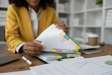 African American businesswoman searching through piles of paperwork for financial, tax, accounting documents on her desk to prepare to explain and clarify at management concept meeting.