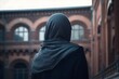 A Muslim woman in a black niqab outfit stands in a courtyard