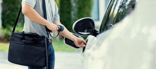 Sticker - Progressive asian man install cable plug to his electric car with home charging station in the backyard. Concept use of electric vehicles in a progressive lifestyle contributes to clean environment.