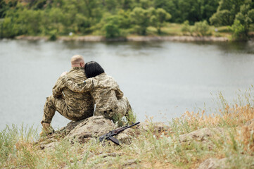 Ukrainian military man and woman are sitting on a stone against the background of the river.