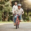 © Siphosethu F/peopleimages.com - Boy with smile on bicycle, father and learn cycling with help, helmet for safety and family in park. Support, motivation and trust, black man and young kid outdoor, teaching and learning bike riding