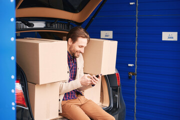 Wall Mural - Young man with cardboard boxes in car trunk at storage warehouse