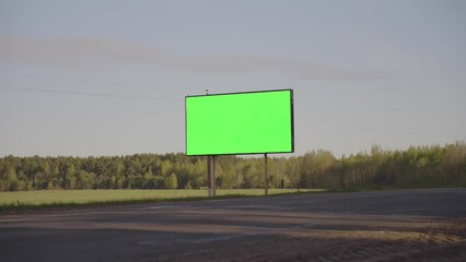 Wall Mural - Large billboard with green chromakey stands on roadside of highway against forest. Advertisement to attract consumer attention. Motorway traffic time lapse