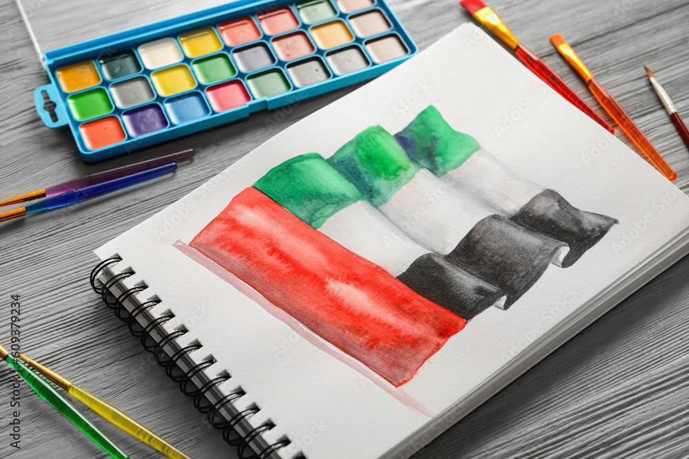 Notebook with drawn UAE flag, brushes and paints on grey wooden background