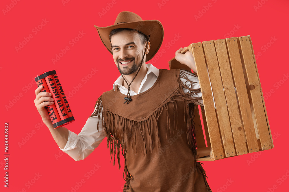 Handsome cowboy with explosive and wooden box on red background