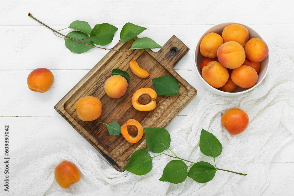 Board and bowl with fresh apricots on white wooden background