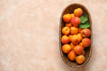 Wall Mural - Wicker bowl with fresh apricots on beige background