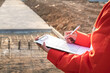 © Nattawit - Action of a civil engineer is checking the building quality report form with construction work site as background. Industrial working action scene with people, close-up and selective focus.