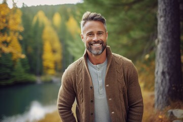 Portrait of handsome mature man smiling at camera while standing in autumn forest