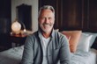 © Robert MEYNER - Cheerful mature man looking at camera and smiling while sitting on bed at home