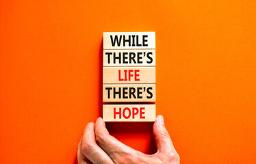 Life and hope symbol. Concept word While there is life there is hope on wooden block. Beautiful orange table orange background. Businessman hand. Business lifestyle life and hope concept. Copy space.