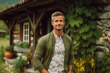 Portrait of a handsome man in a green jacket standing in front of a rustic cottage