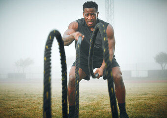 Fitness, battle rope and black man on field for power workout, body building and training muscle strength. Exercise, sports and African bodybuilder on grass with ropes, energy and outdoor performance