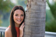 © @skuder_photographer - Young and beautiful woman leaning on the trunk of a palm tree. Woman is happy and relaxed and enjoying the sunny day in seville, spain. The woman is wearing jeans and orange top.