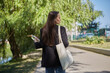 © hurricanehank - Beautiful young woman walking in the green park with a glass bottle of water in hand and cotton tote bag on a shoulder. Responsible and trendy female person on a walk
