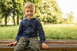 © kieferpix - A smiling toddler blond boy sits on park bench, looking at camera.