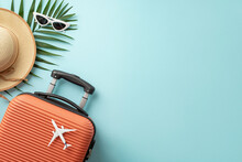 Summer Getaway Concept. Top View Of An Orange Suitcase, Small Airplane Figurine, Beach Essentials, Sunglasses, Sunhat, Palm Leaves On Pastel Blue Background, Providing Space For Text Or Promo Content