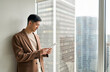 © insta_photos - Professional young Asian businessman using tablet standing at window. Japanese business man executive working with fintech device, checking digital marketing ecommerce business project.
