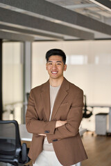 Young happy Asian business man looking at camera standing in office. Smiling confident professional Japanese businessman executive, company employee or entrepreneur wearing suit, vertical portrait.