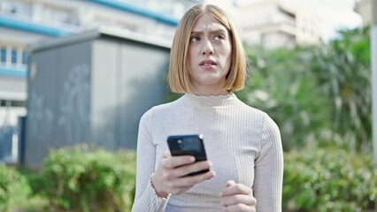 Wall Mural - Young blonde woman using smartphone with serious expression at park