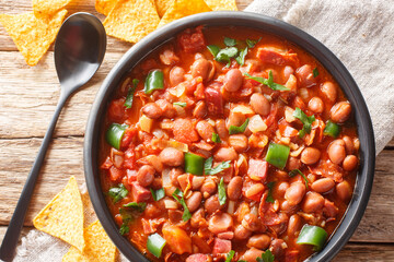 Canvas Print - Mexican pinto bean stew with tomatoes, sausages, bacon and onions close-up on a bowl on the table. horizontal top view from above