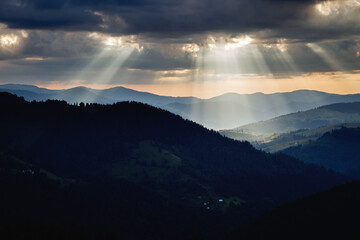 Wall Mural - a solar spotlight shines through the dark ominous clouds on the mountain slopes.