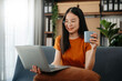 © laddawan - Asian woman using the smartphone and tablet on the sofa at home.