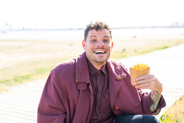 Wall Mural - Young caucasian man holding fried chips at outdoors with surprise and shocked facial expression