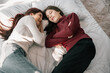 Asian lesbian partners smile, relax, laugh, affectionately pinch and kiss each other's cheeks while lying on the bed. A combination of personal charm, a good sense of humor, and a romantic moment.