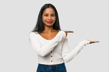 Wall Mural - Young Indian woman cut out isolated on white background excited holding a copy space on palm.