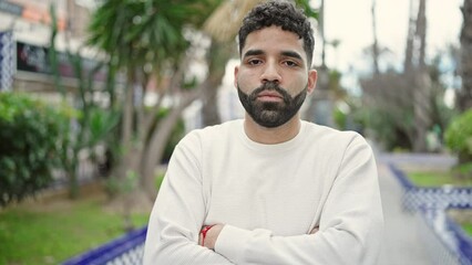 Sticker - Young hispanic man standing with serious expression and arms crossed gesture at park