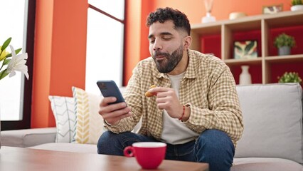 Sticker - Young hispanic man having breakfast using smartphone at h